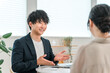© buritora - 商談テーブルで女性顧客と打ち合わせ,カウンセリング,ヒアリングをする若いアジア人ビジネスマン