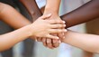 © Studicon - Four individuals with varying skin tones are shown with their hands stacked on top of each other, symbolizing unity and teamwork.