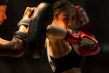Confident female Muaythai boxer practicing Thai boxing with male trainer in gym