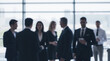 © Dmytriy - Blurred image of a group of people in business attire talking in a modern office with large windows and city view