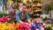 © mila103 - A florist carefully arranges colorful flowers in a lively flower shop filled with various blooms. The shop is bright and inviting, showcasing a diverse selection of petals and plants.