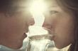 © lemonmoon - Close up of couple drinking water together outdoors, sunlight shining between faces, romantic and intimate moment, clear glass, hydration, healthy lifestyle, young adults