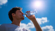 © Curioso.Photography - Young man hydrating under bright sun with clear blue sky and clouds in the background.
