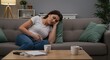 © Farhan - Woman with abdominal pain sitting on the couch at home.