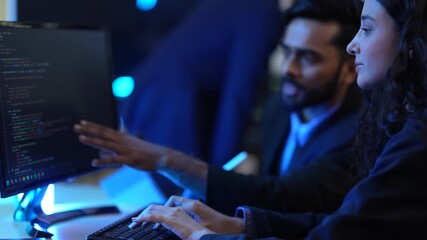 Two colleagues work together late at night in a modern office. The man discusses an idea while the woman types on the keyboard, collaborating on an important project.