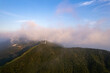 Jiugong Mountain in Xianning City, China features wind turbines on its green peaks, nestled among soft clouds under a blue sky.