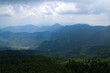 Jiugong Mountain in Xianning City, China stretches across the horizon under a cloudy sky, showcasing vast green slopes and a valley below.