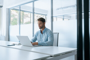 European businessman entrepreneur using computer technology app for work online. Young professional specialist latin hispanic business man working on laptop pc sitting at desk in office. Copy space