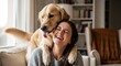 © ALLmost - A happy young woman laughs with joy as her affectionate golden retriever dog hugs her from behind on the couch at home.