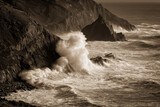 Dramatic ocean wave crashing against rugged cliff powerful water spray rocky coastline moody atmosphere nature force monochrome dynamic seascape wild sea erosion energy