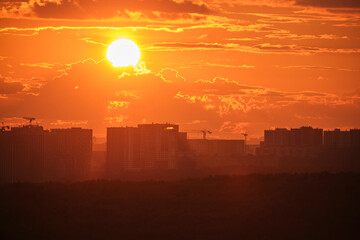 Wall Mural - Vivid orange sunset over city skyline with high-rise buildings and construction cranes, casting dramatic silhouettes against glowing clouds and sky.