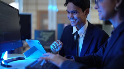 A male and female programmer collaborate on a software project. The team leader is training a new intern, explaining the code on her screen in the tech office after hours.