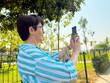 © satura_ - Woman taking a photo outdoors with a smartphone in her hands. Daily life, urban leisure, and personal perspective in an open park environment.