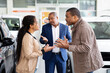 © Anastasiya - Young African American couple arguing in car showroom while dealer watches, conflict about purchase decision, lifestyle scene of disagreement and relationship stress