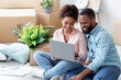© Prostock-studio - Smiling millennial african american wife showing to husband laptop with new room design, sitting on floor with boxes and plants. Couple planning interior of apartment, moving and buying furniture