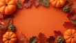 © Maria - a frame of pumpkins and colorful autumn leaves on an orange background, creating copy space for text or design in the center.