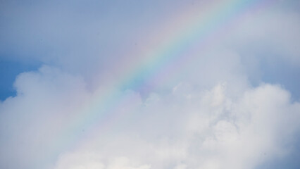 Wall Mural - Rainbow in the blue sky with white clouds and copy space.