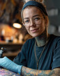 © Pedro - A portrait of a woman with tattoos in the studio. She wears glasses and has a focused expression on her face, holding the tattoo machine
