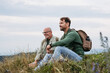 © Halfpoint - Adult son and older father hiking togeter in nature, resting on meadow.