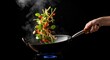 © Artha - A person tossing fresh vegetables and noodles while cooking in a wok over a gas flame.