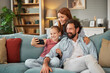 © Stockphotodirectors - A family sits together on a comfortable couch, capturing a joyful selfie. They are surrounded by cozy decor, sharing smiles and laughter in their inviting living room.