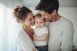 © Crowded Studio - El amor nace en brazos que sostienen, en miradas que protegen y comparten la vida. Tres personas en una habitación luminosa; un adulto sostiene a un bebé mientras otro sonríe a su lado.