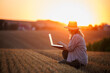 © encierro - Woman agronomist analyzing smart farming data on laptop after harvest on agricultural field during sunset