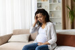 © Anastasiya - Thoughtful pregnant woman sitting on sofa, touching her head with concern. Concept of stress, prenatal headache, and maternity health, copy space