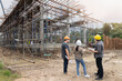 © skarie - Team of engineers and architects wearing safety helmets discussing building progress at construction site with scaffolding structure.