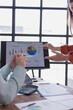 © Tj - Business colleagues analyzing sales data on a computer screen, discussing revenue and profits, using charts and graphs for strategic decision-making in a modern office environment