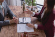 © Tj - Female lawyer discussing contract terms with a client while seated at a wooden table. A tablet, gavel, and statue of Themis, goddess of justice, enhance the legal atmosphere