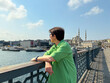 © satura_ - Woman in green dress looking at the Bosphorus from Galata Bridge. Contemplation, travel, and urban lifestyle by the sea.