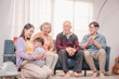 © Thitiporn - Asian multigenerational family spending quality time together at home. Mother hugging toddler with love while others smile and clap, showing strong emotional family connection.