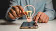 © Prosenjit - Illuminating Innovation: A person interacting with a glowing lightbulb icon on a smartphone, symbolizing modern innovation and idea generation.
