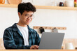© Prostock-studio - Modern remote job of blogger or employee and heath care during covid-19 lockdown. Cheerful asian young man in glasses works at laptop on table with coffee and water in boho style kitchen interior