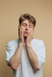 © bodnarphoto - Young man expressing fatigue while resting his face with both hands on a plain background