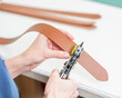 © Михаил Решетников - A woman makes holes in a leather belt. Leatherworker's workshop.
