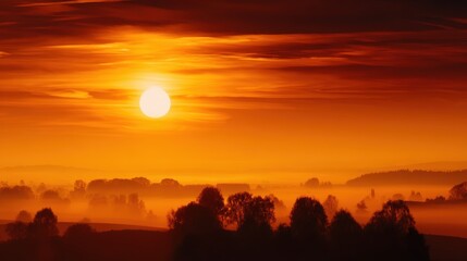 Wall Mural - Serene sunset over a misty landscape, with vibrant orange hues illuminating the horizon and trees
