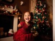 © afr - Happy little girl in red dress smiling near Christmas tree with fireplace garlands, warm family holiday atmosphere