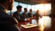 © justholla - Business meeting in a modern office with a focus on a bearded man and a notebook on a polished table, sunlight streaming through large windows at sunset