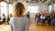 © Suphitcha - Woman speaking to audience in conference room with wooden floor and bright windows