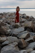 © Сергей Луговский - Beautiful slim young woman in long red dress standing on stones at the sea