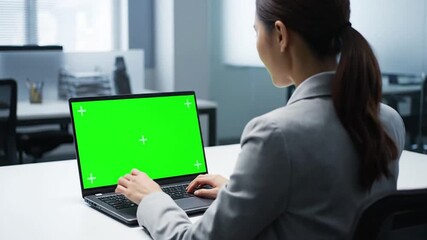 Focused woman using laptop with green screen display in a bright modern workspace for creative digital projects