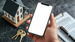 © chekart - Housing insurance. Rent, sale and purchase of a country house. Mobile app advertising. A mockup of the phone in the male hand of a real estate agent. There is a miniature house on the table
