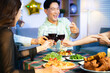 © Nuttapong punna - Closeup of smiling friends toasting with red wine at a lively indoor party table, sharing food, laughter, and joyful moments in a cozy