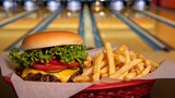 Juicy cheeseburger and golden french fries served in a basket at a lively bowling alley entertainment venue