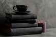 © Oksana Smyshliaeva - Stack of Black Books with Coffee Cup and Candle on Gray Background.