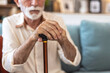 © Jelena Stanojkovic - Walking stick, hands and senior man with a disability in home, apartment or retirement with support for injury. Elderly, closeup or person with wood cane to help balance or mobility with arthritis.