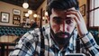 © maxximmm - Man with beard looking at his phone. Man in a plaid shirt is thinking. A cafe sitting indoors with a beautiful atmosphere. A bearded man gazing at his phone lifestyle.