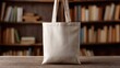 © Momin Photo Gallery - Elegant photo of beige canvas tote bag mockup template on wooden table in library. Eco friendly totebag mock up made of natural cotton. Reusable shopper ecobag canvas for design.